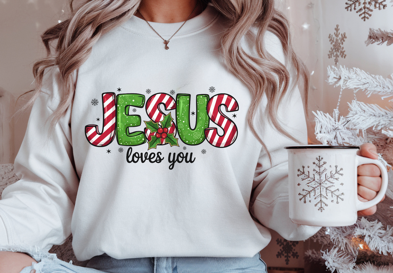 Person wearing a white sweatshirt with 'Jesus loves you' text, holding a mug with a snowflake design.